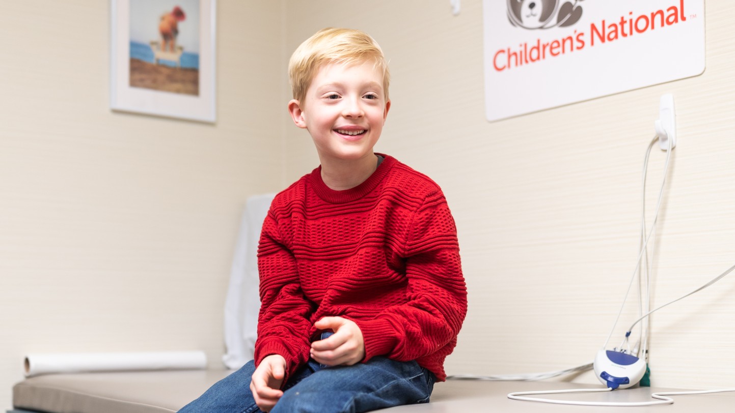Young boy smiling while sitting on exam table in patient care room