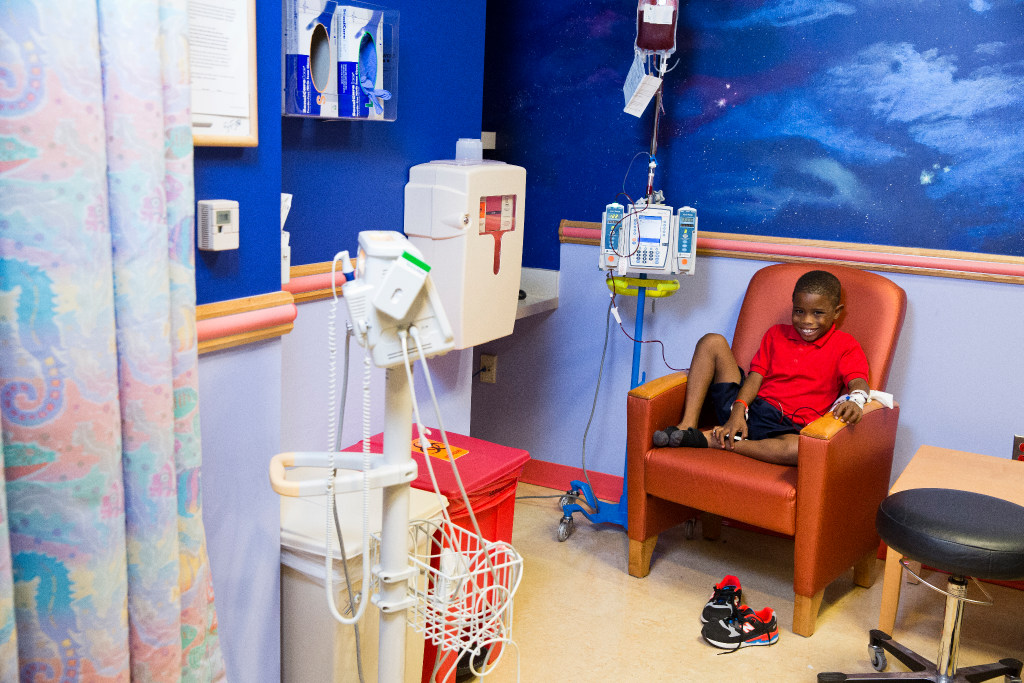 Smiling boy patient sitting on a chair in hospital room with medical equipment
