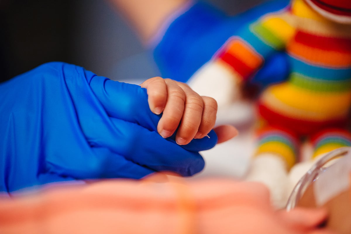 Adult Hand in Glove holding a Baby's Hand.