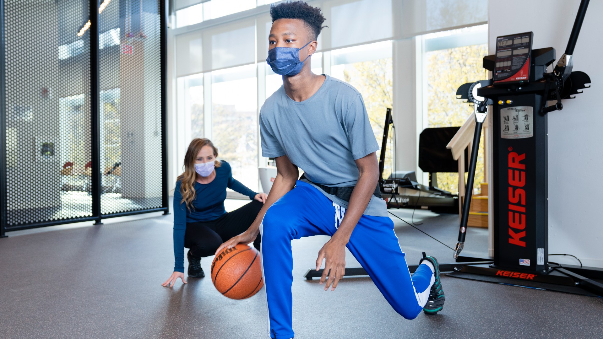 Teenage boy dribbling a basketball while Physical Therapist observes