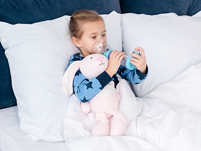 little girl in bed using asthma inhaler