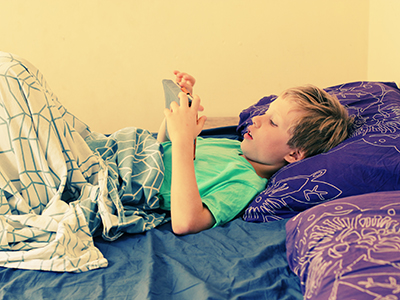 boy lying in bed using tablet